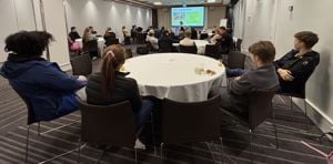 Ei gruppe elevar (tillitsvalde) samla ved fleire runde konferansebord følger med på presentasjonen til elev- og lærlingomboda